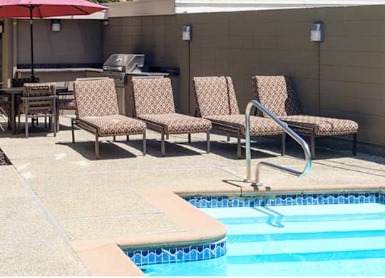 A pool with a red umbrella and chairs around it.