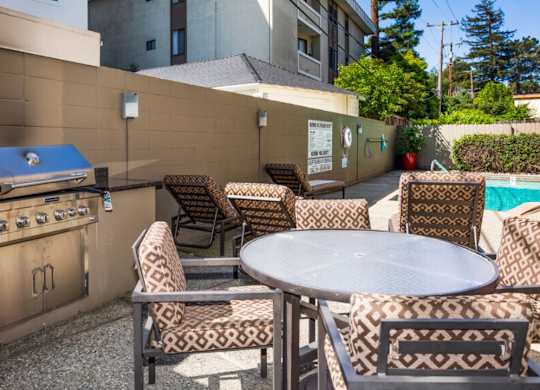 A patio with a table, chairs, and a grill.