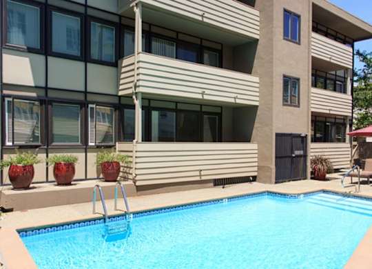 A swimming pool in front of a building with a red umbrella.