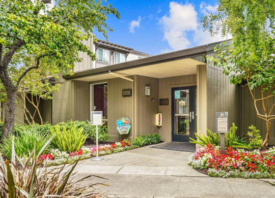 the entrance to a green building with a sidewalk and trees
