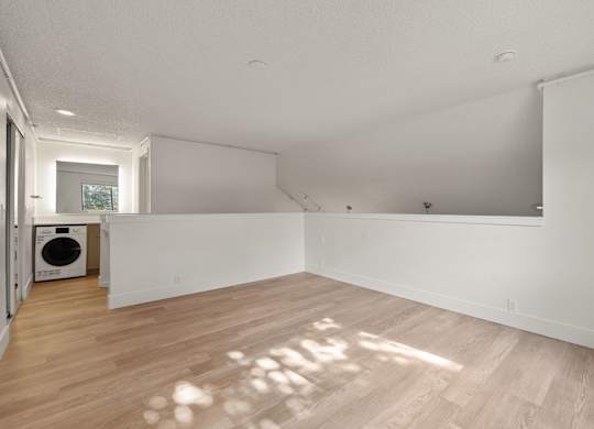 the living room and laundry room of a renovated house with white walls and wood floors at AVIA Lofts on Parkway Apartments, Washington, 98662