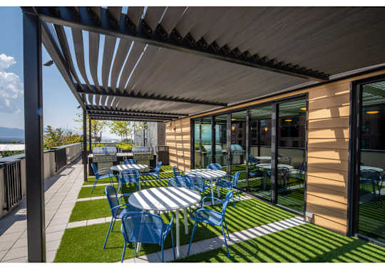 A patio with blue chairs and a table is covered by a roof.