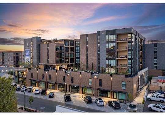 A modern multi-story building with a parking lot in front.