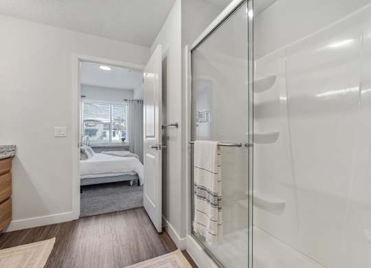 a white bathroom with a glass shower and a bedroom at The Flats at Riverwoods, Provo, Utah