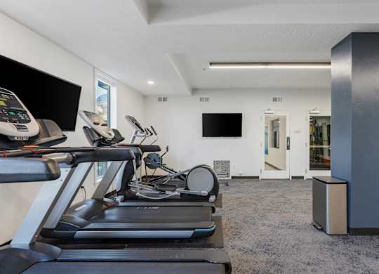 the gym has cardio equipment and a flat screen tv at The Flats at Riverwoods, Provo, UT, 84604