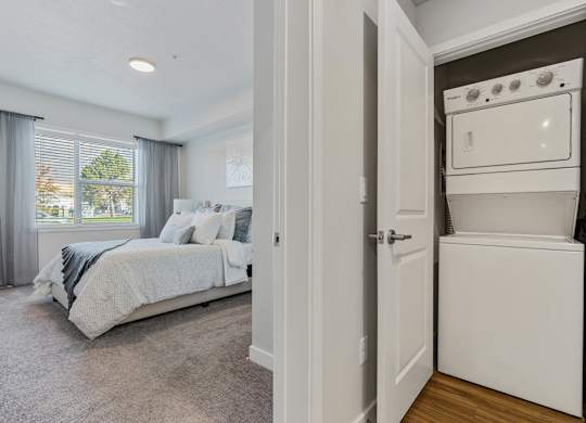 a bedroom with a bed and a washer and dryer next to a closet at The Flats at Riverwoods, Provo, Utah
