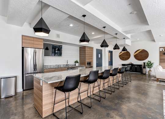 a kitchen with a long island with black chairs and a stainless steel refrigerator at The Flats at Riverwoods, Provo