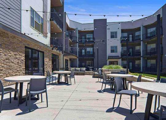 a patio with tables and chairs in front of an apartment building at The Flats at Riverwoods, Provo, 84604