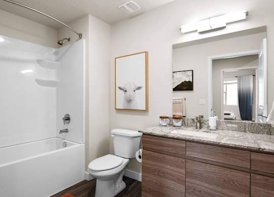 a bathroom with a white bathtub and a white toilet next to a sink with a mirror at The Flats at Riverwoods, Provo, UT, 84604