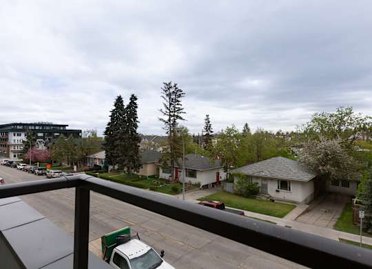 A view of a street from a balcony with a white van and a green truck.