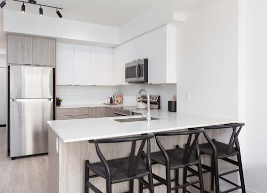 A modern kitchen with a white countertop and black chairs.