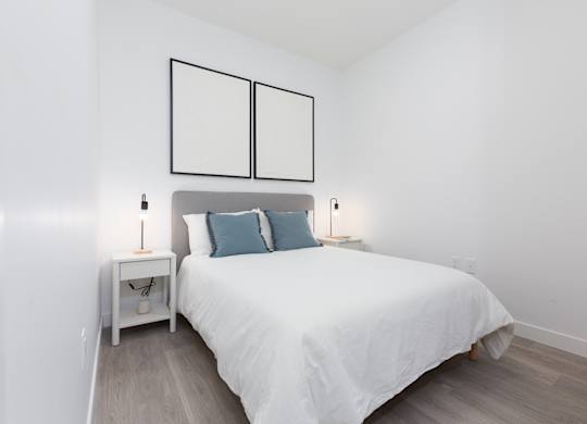 A white bed with a white nightstand and a white bedroom.