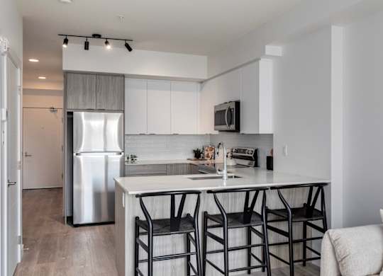 A modern kitchen with a white island and black barstools.