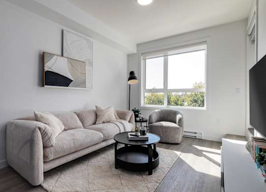 A living room with a grey couch, a black coffee table, and a large window.