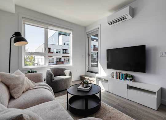 A living room with a large window, a grey sofa, a black coffee table, a white TV stand, and a floor lamp.