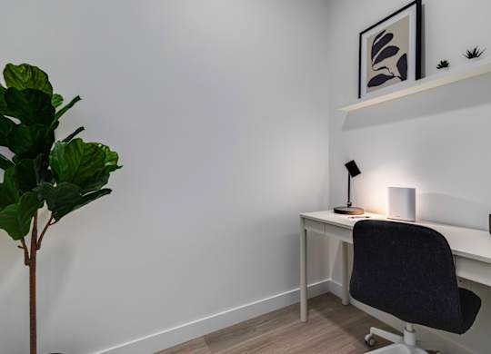 A small desk with a black chair and a lamp on it.