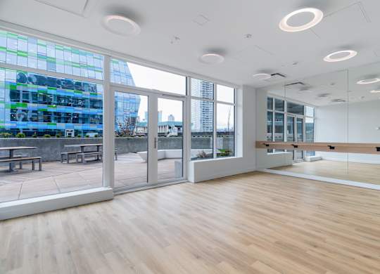 A spacious room with wooden floors and large windows overlooking a cityscape.