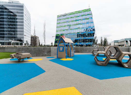 A playground with a blue and yellow surface and a green building in the background.