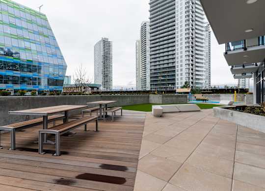 A wooden table and benches are on a patio in front of a building.