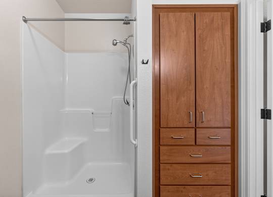 A white shower stall with a glass door and a wooden cabinet with drawers.