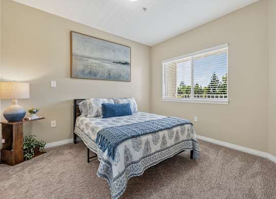A bedroom with a bed, lamp, and painting on the wall.