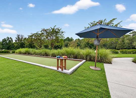 A blue umbrella stands on a concrete slab in a grassy area.