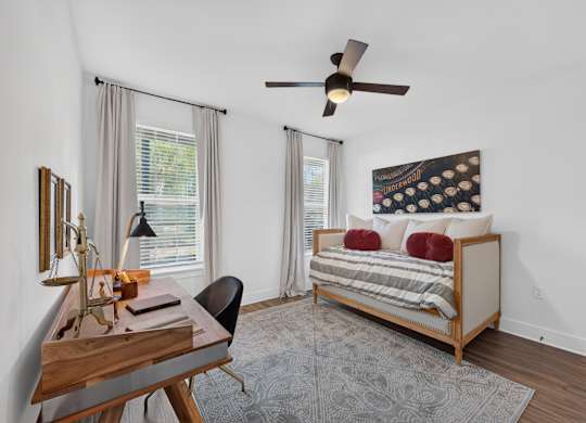 A bedroom with a bed, a desk, and a ceiling fan.