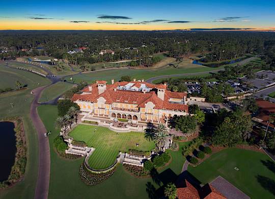 A large, beautifully designed building with a red roof is surrounded by a well-kept lawn and a winding path.