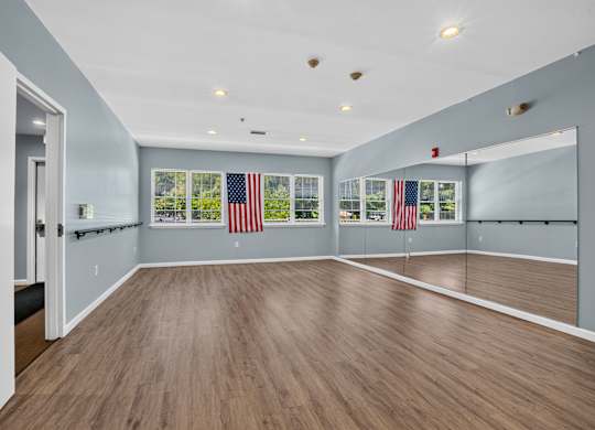 A spacious room with wooden flooring and American flags on the windows.