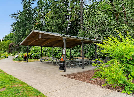 A picnic area with a shelter and tables surrounded by greenery.