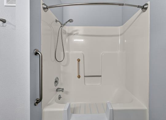 A white bathtub with a shower head and hand held shower. Curved shower curtain rod, hand rails for easy entry and exit.
