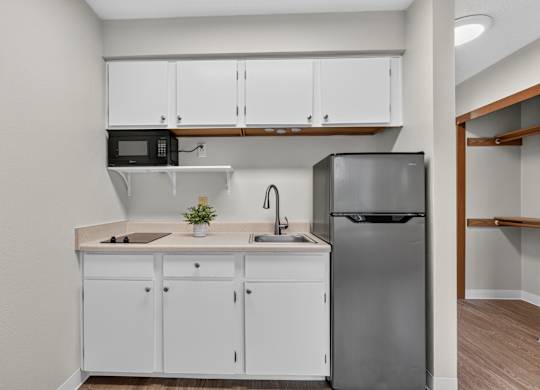 A kitchen with white cabinets and a black fridge. Kitchenette style with beige walls