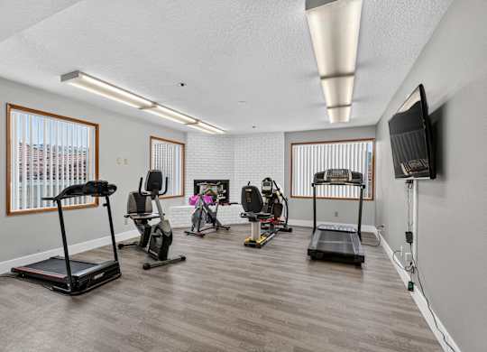 Fitness center with a treadmill, exercise bike, and other equipment. Also a tv mounted on the wall.