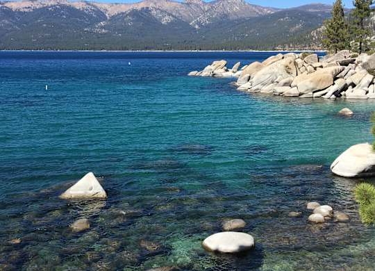 A serene lake with clear water and rocks in the foreground.