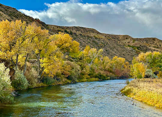 A river flows through a valley with trees showing autumn colors.