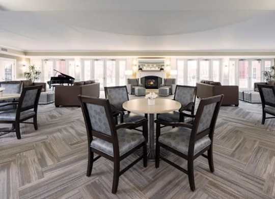 A room with a table surrounded by chairs and a piano in the background.
