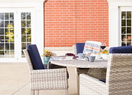 A table with chairs and a potted plant on a patio.