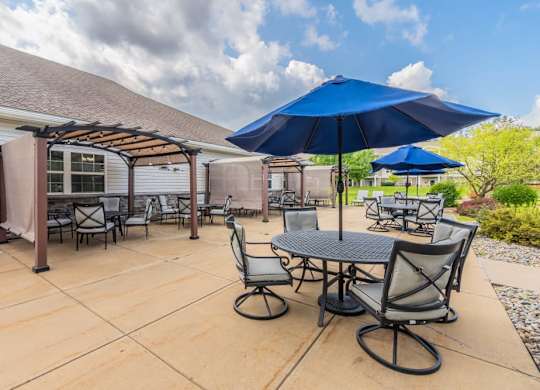 Outdoor dining patio with pergola and umbrellas at Schuyler Commons Apartments, Utica, 13502