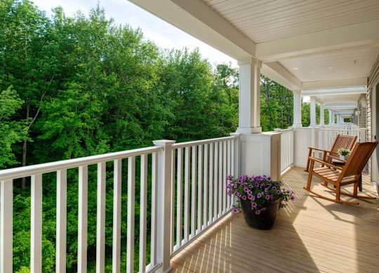 Covered balcony with rocking chairs and forest view at Glenmont Abbey Village, 55+ Apartments, Glenmont, NJ 12077