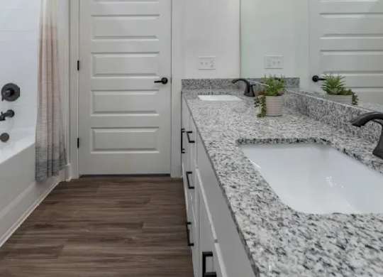 A bathroom with a white door, a marble countertop, and a plant on the counter. at Atwater at Nocatee Apartments, Toledo