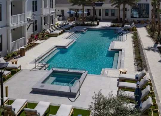 A large swimming pool surrounded by lounge chairs and palm trees. at Atwater at Nocatee Apartments, Florida