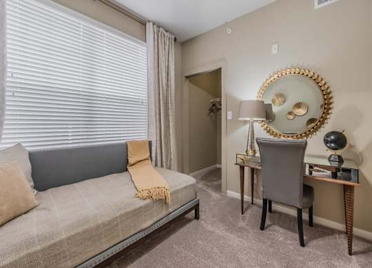 A living room with a grey couch, a chair, and a desk with a lamp. at The Spring at Silverton Apartments, Fort Worth