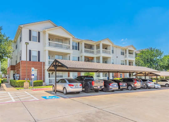 A sunny day at a multi-story apartment complex with cars parked in the lot. at The Spring at Silverton Apartments, Texas