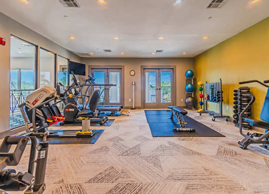 A well-equipped gym with a variety of exercise machines and a blue mat for floor exercises. at The Spring at Silverton Apartments, Fort Worth, 76133