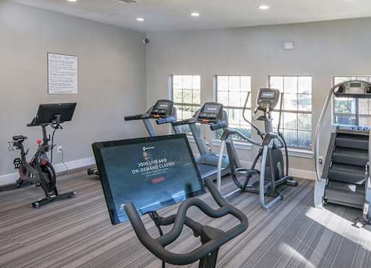 A gym with treadmills, exercise bikes, and a television screen showing a fitness program.