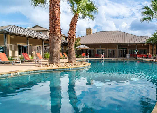 A pool surrounded by palm trees and a building in the background.