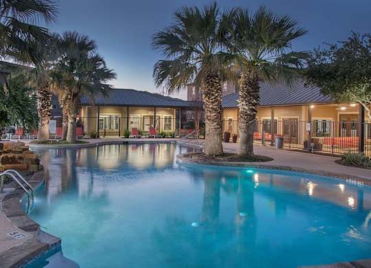A pool surrounded by palm trees at night.