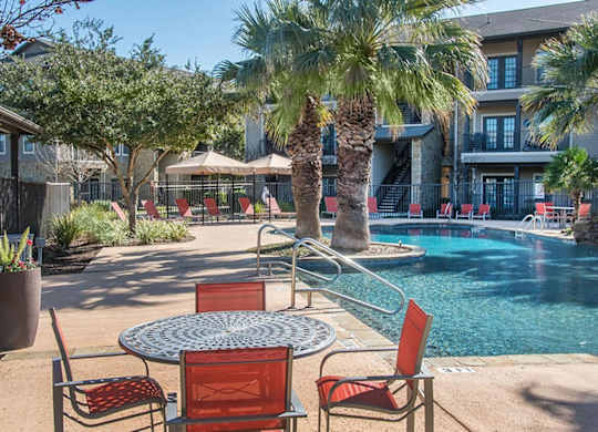 A poolside table with chairs is surrounded by palm trees.