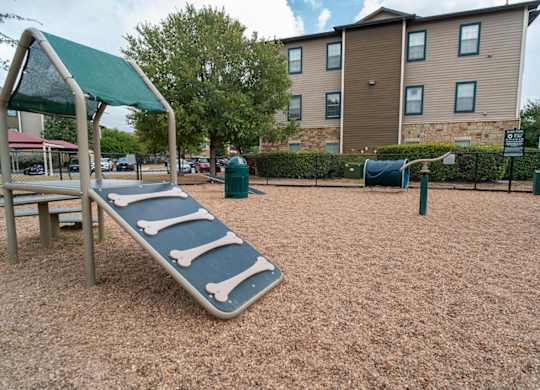 A playground with a slide and a building in the background.