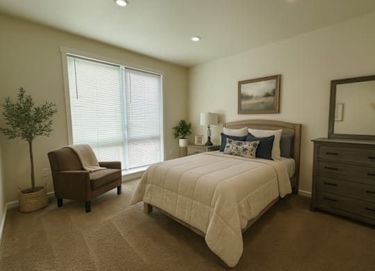 A well-lit bedroom with a large bed, a chair, and a potted plant.